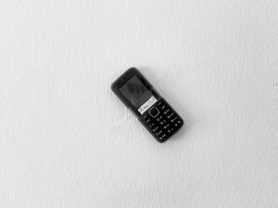 A small keypad mobile phone taped to a bare white wall.